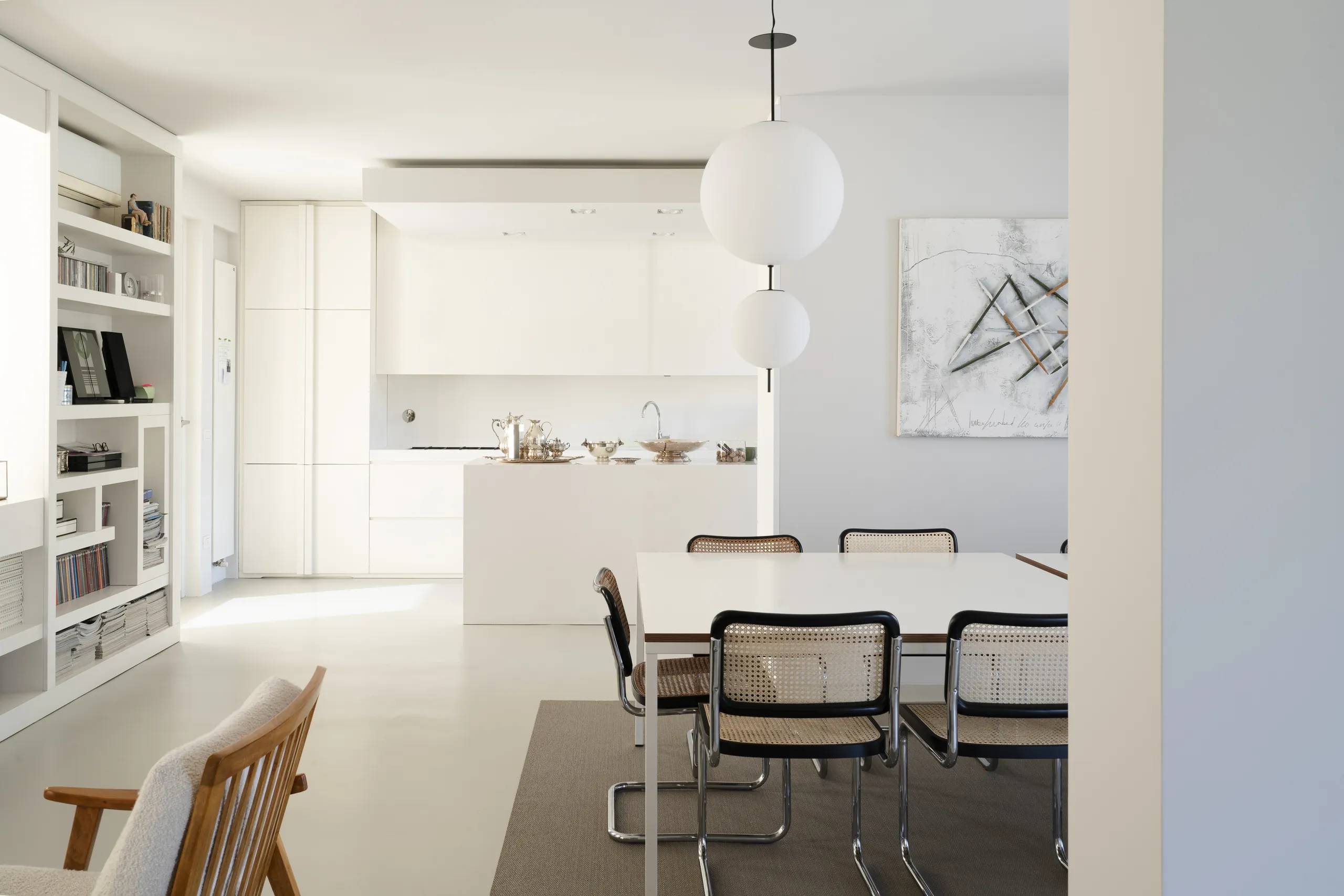 Interno contemporaneo luminoso: zona pranzo con sedie in paglia di Vienna e cucina bianca minimale